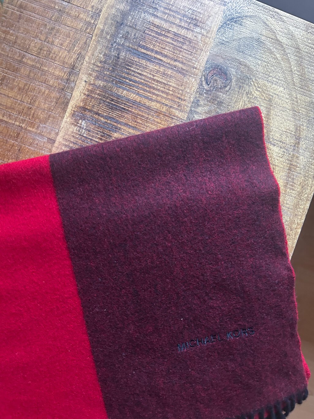 Grosser Kaschmir Schal von Michael Kors preloved und modern. Zweifarbig in Rot und Bordeaux, gefaltet auf Holztisch.