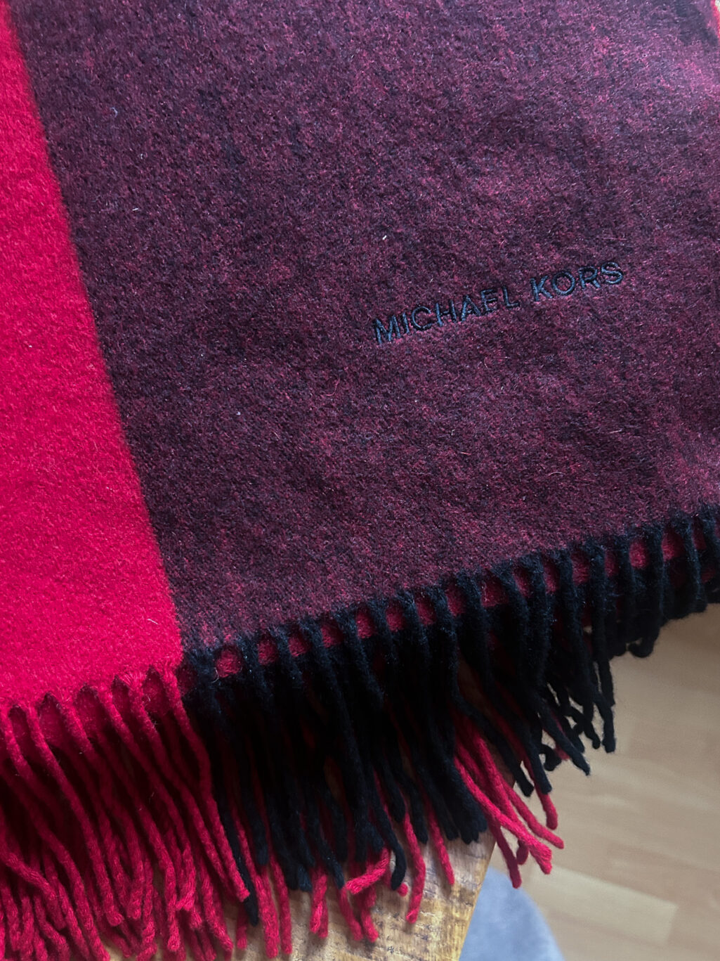 Grosser Kaschmir Schal von Michael Kors preloved und modern. Zweifarbig in Rot und Bordeaux, gefaltet auf Holztisch.