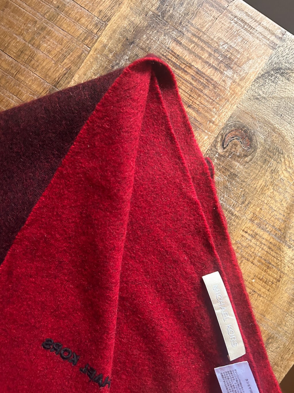 Grosser Kaschmir Schal von Michael Kors preloved und modern. Zweifarbig in Rot und Bordeaux, gefaltet auf Holztisch.