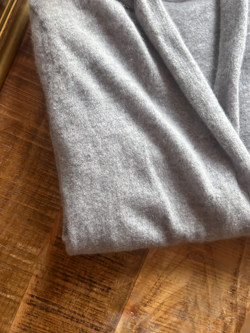 Tissaia, preloved 100% Cashmere Cardigan in Grau, gefaltet auf Holztisch.