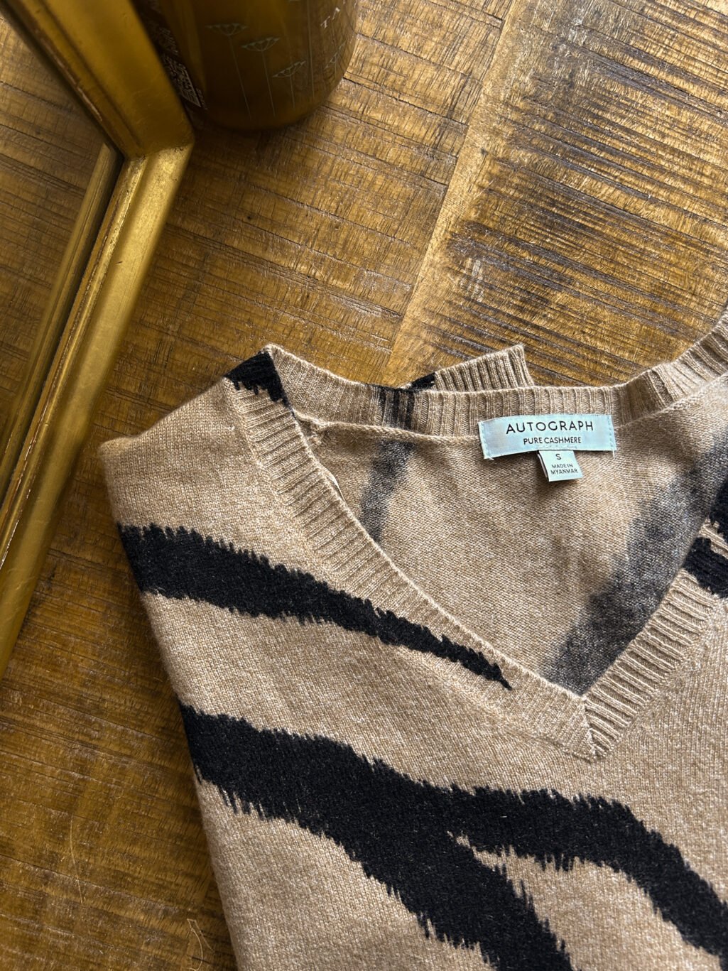 Cashmere Pullover von Autograph mit V-Neck in Beige / Braun mit Animal Print. Secondhand gefaltet auf Holztisch.