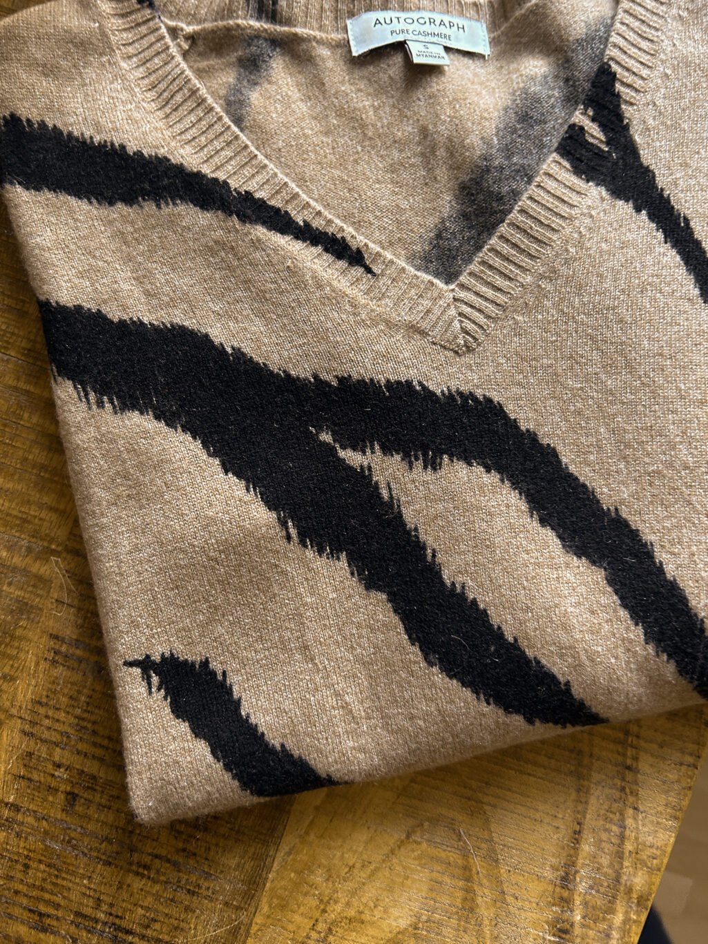 Cashmere Pullover von Autograph mit V-Neck in Beige / Braun mit Animal Print. Secondhand gefaltet auf Holztisch.