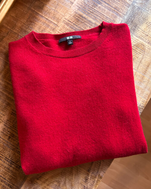 Secondhand Kaschmirpullover von Uniqlo in Rot. Gefaltet auf Holztisch.