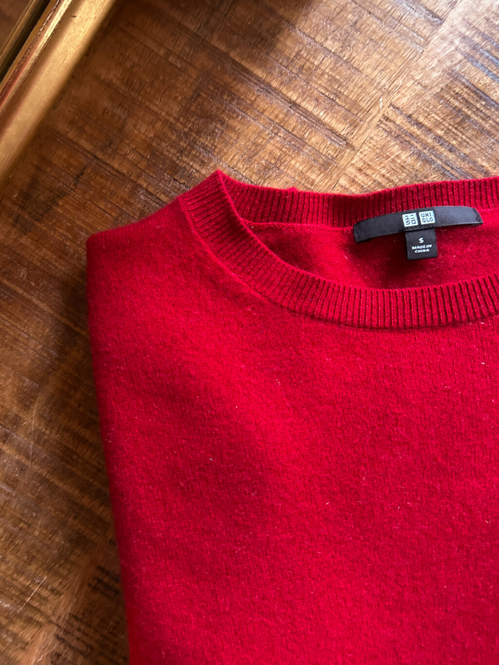 Secondhand Kaschmirpullover von Uniqlo in Rot. Gefaltet auf Holztisch.