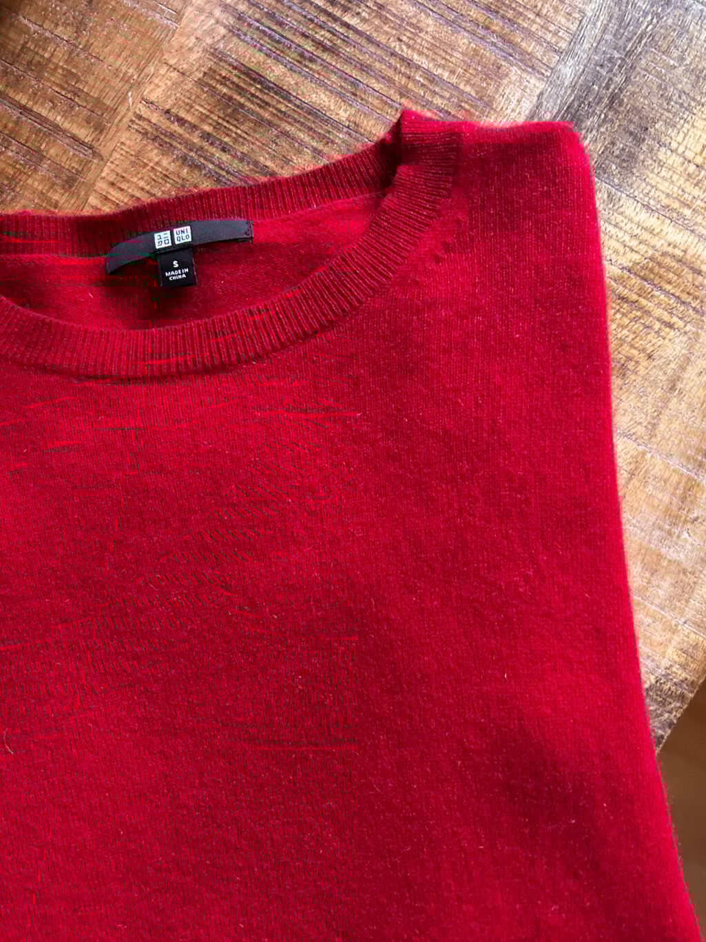 Secondhand Kaschmirpullover von Uniqlo in Rot. Gefaltet auf Holztisch.
