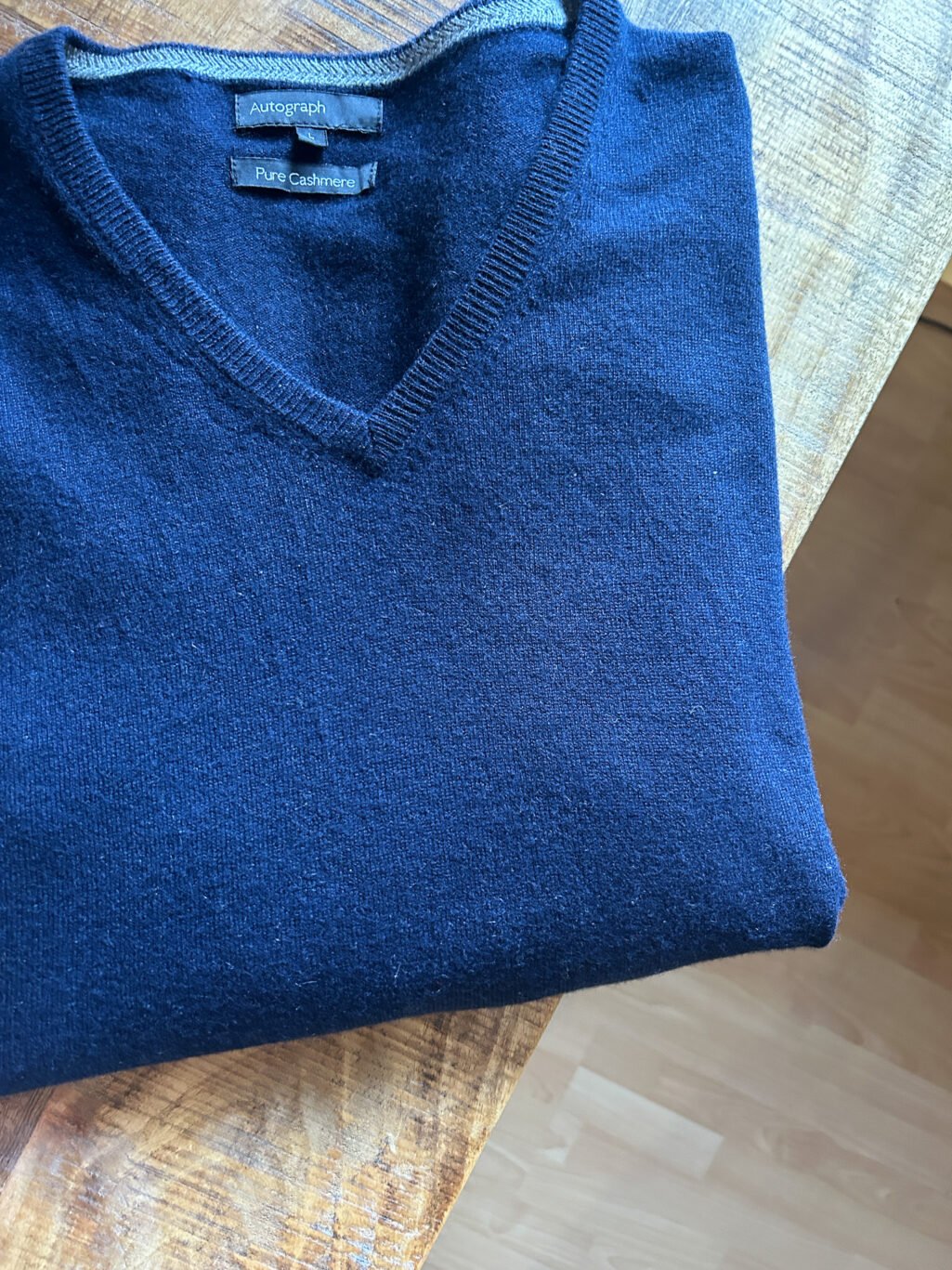 Blauer Autograph Cashmere Pullover mit V-Neck f&uuml;r Herren. Gefaltet auf Holztisch.